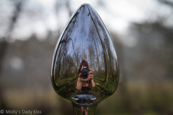 Person taking picture reflected in the head of metal butt plugs