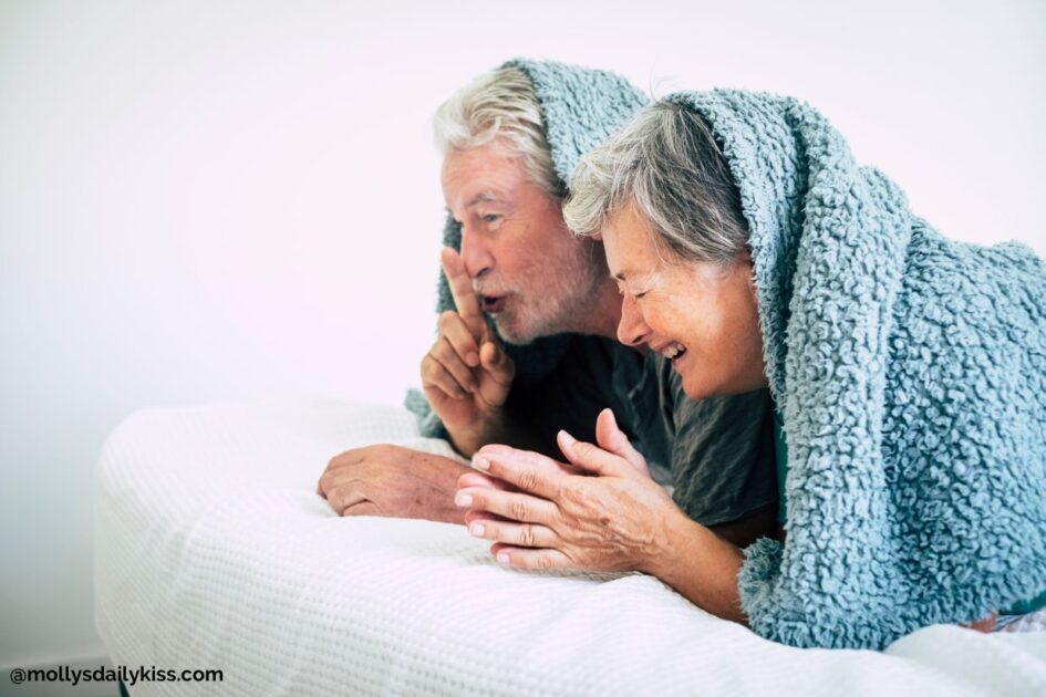Older white couple laying in bed with blanket over the head laughing for post about laughter